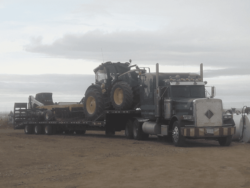 semi trailer hauling a green tractor and pieces of equipment